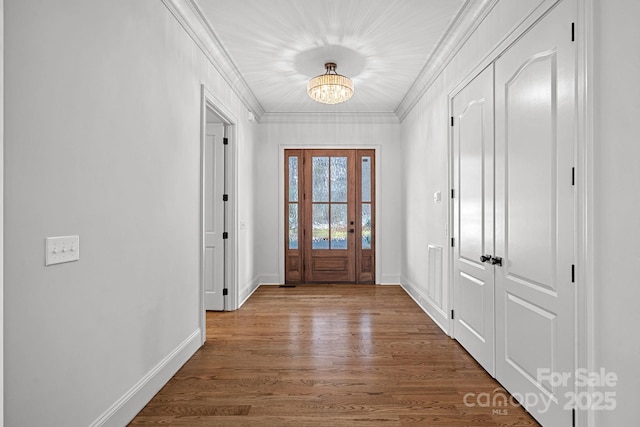 entryway with an inviting chandelier, baseboards, crown molding, and wood finished floors