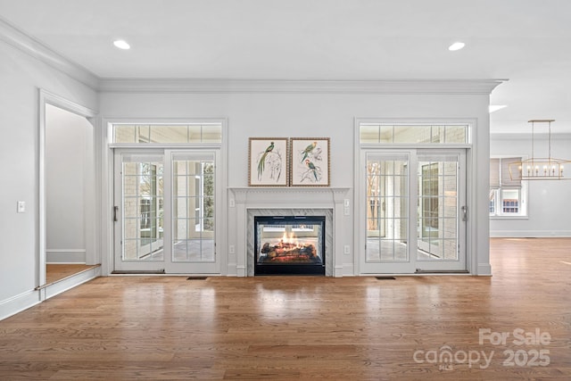 unfurnished living room with a fireplace, crown molding, wood finished floors, and a chandelier