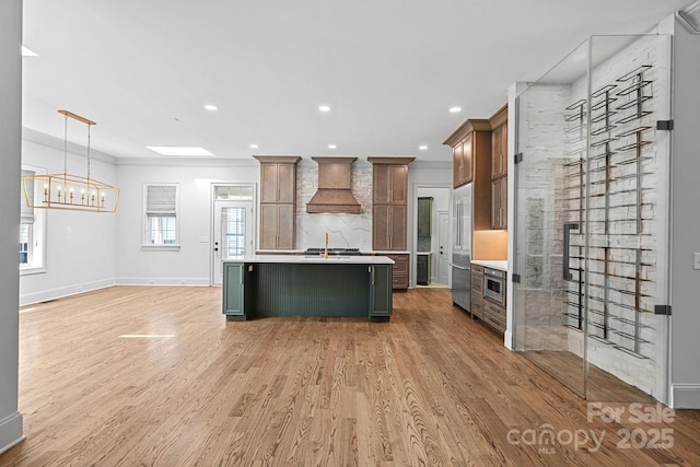 kitchen with light countertops, custom range hood, light wood finished floors, and ornamental molding