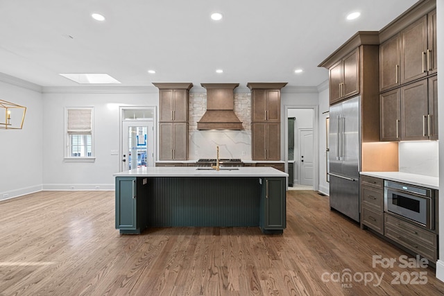 kitchen featuring wood finished floors, custom exhaust hood, ornamental molding, light countertops, and built in appliances