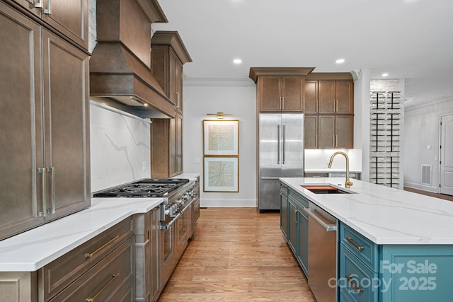 kitchen with premium range hood, ornamental molding, a sink, light wood-style floors, and appliances with stainless steel finishes