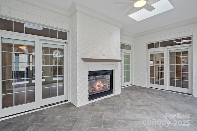 unfurnished living room with a ceiling fan, brick wall, a skylight, ornamental molding, and a brick fireplace