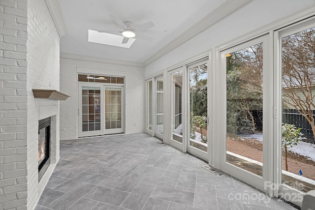 unfurnished sunroom with a brick fireplace, a skylight, and a ceiling fan