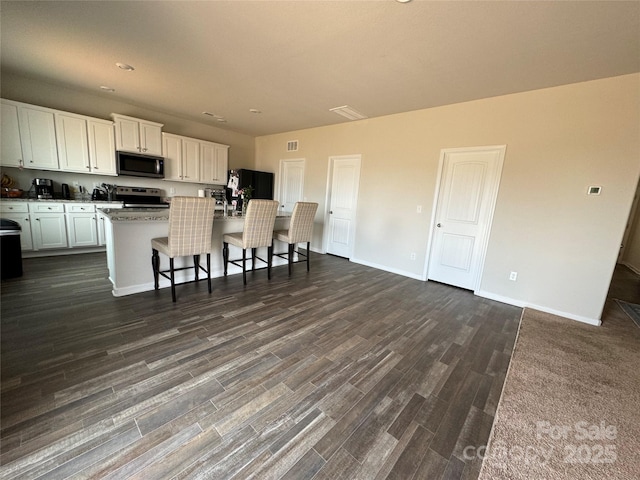 kitchen with a breakfast bar, white cabinets, a center island, stainless steel appliances, and dark wood-type flooring