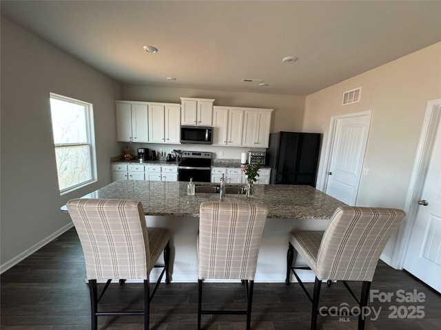 kitchen featuring sink, white cabinetry, appliances with stainless steel finishes, an island with sink, and light stone countertops