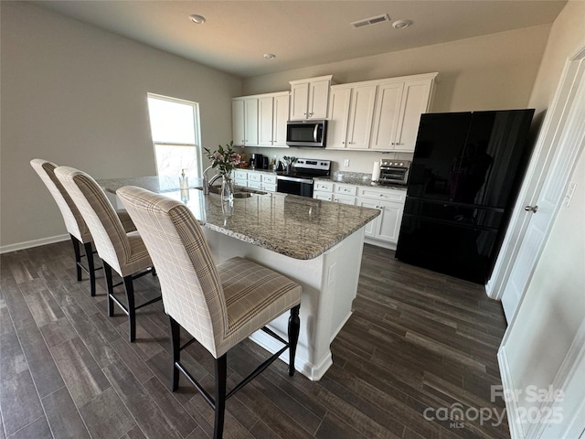 kitchen with appliances with stainless steel finishes, an island with sink, dark stone counters, and white cabinets