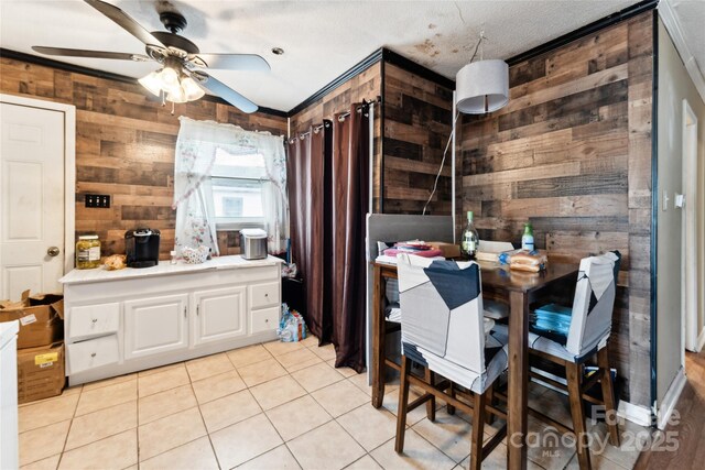 dining space with light tile patterned flooring, ceiling fan, and wood walls