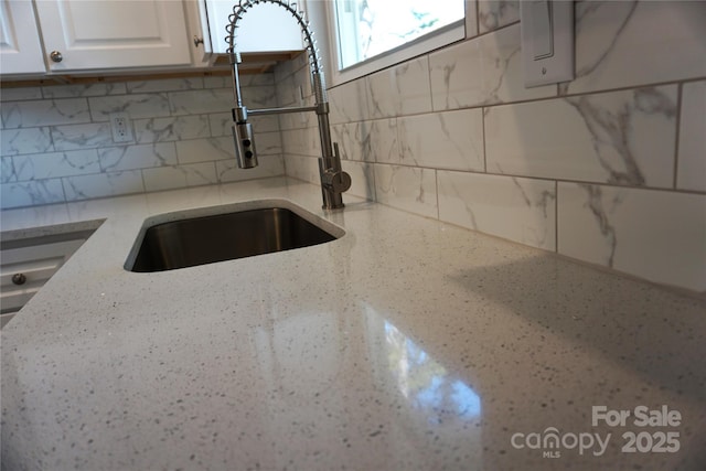 kitchen with tasteful backsplash, sink, white cabinets, and light stone counters