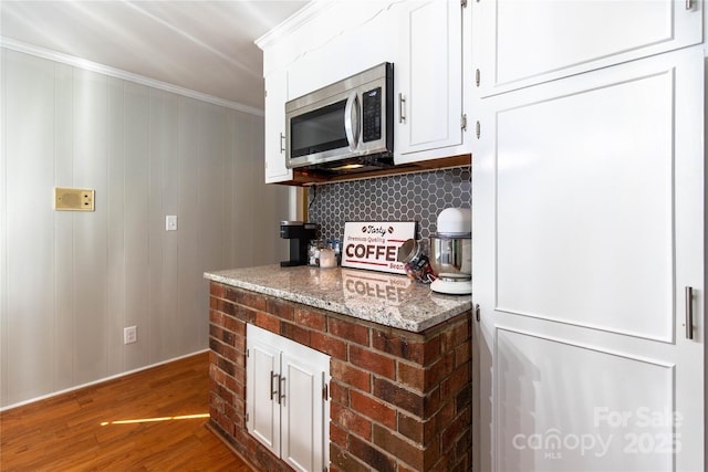 kitchen featuring hardwood / wood-style flooring, crown molding, white cabinets, and light stone counters