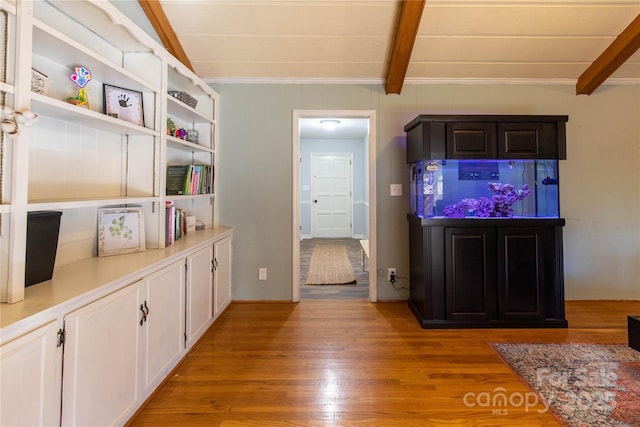 kitchen with lofted ceiling with beams, ornamental molding, white cabinets, and light wood-type flooring