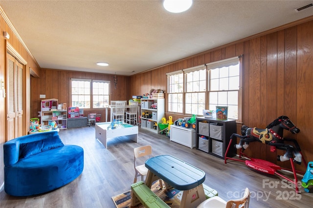 playroom featuring hardwood / wood-style flooring, ornamental molding, a textured ceiling, and wood walls