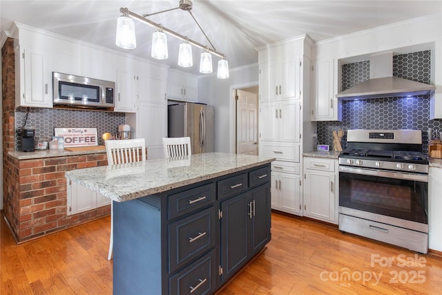 kitchen featuring tasteful backsplash, wall chimney range hood, white cabinets, and appliances with stainless steel finishes