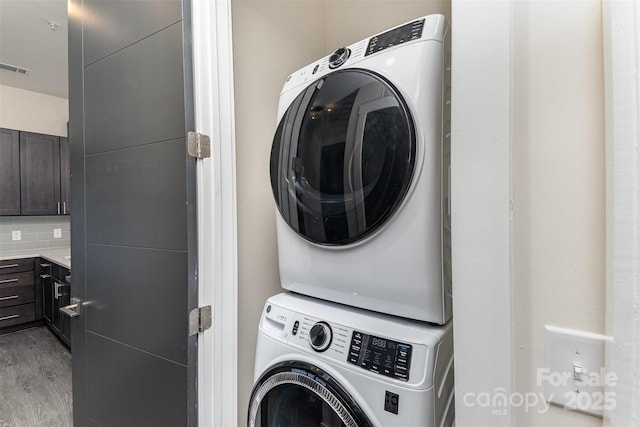 laundry area with stacked washing maching and dryer and light hardwood / wood-style floors