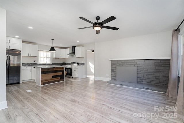 kitchen with wall chimney exhaust hood, white cabinetry, black refrigerator, stainless steel range, and pendant lighting