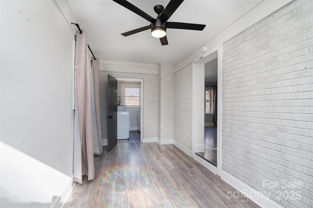 hallway with crown molding, wood-type flooring, brick wall, washer / clothes dryer, and a barn door