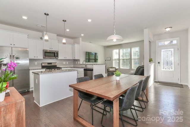 interior space featuring hanging light fixtures, a kitchen island, white cabinets, and appliances with stainless steel finishes