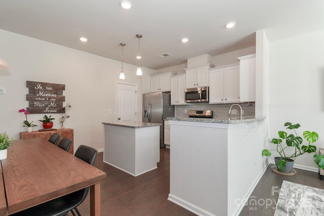 kitchen featuring light stone counters, appliances with stainless steel finishes, kitchen peninsula, and hanging light fixtures