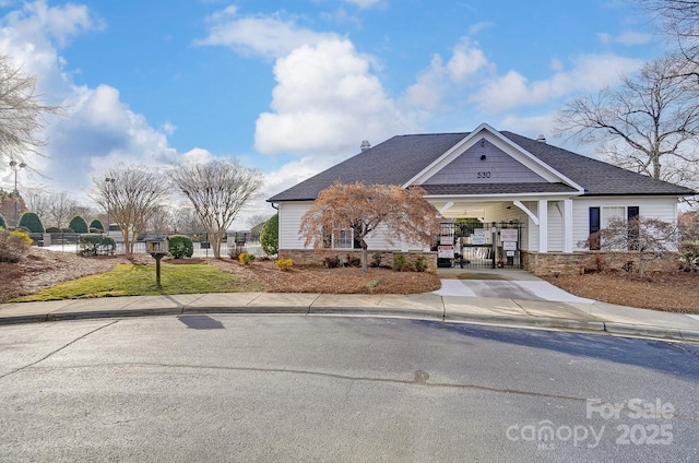 view of front of home with stone siding, fence, concrete driveway, and roof with shingles