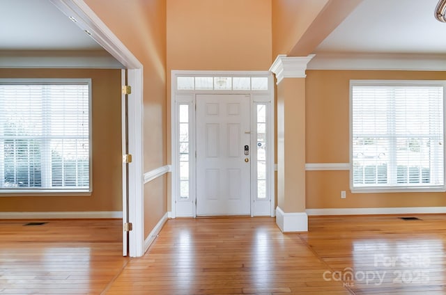 foyer entrance with ornamental molding, a wealth of natural light, and ornate columns