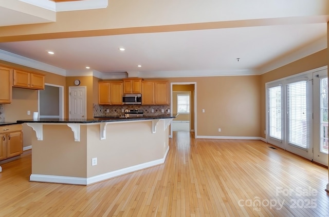 kitchen featuring appliances with stainless steel finishes, a breakfast bar, light wood-style floors, and decorative backsplash