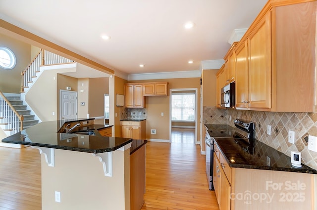 kitchen featuring a breakfast bar, crown molding, stainless steel appliances, a sink, and light wood-type flooring