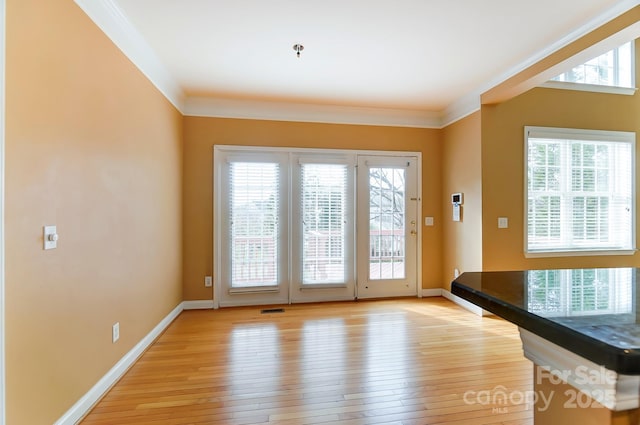 doorway featuring light wood finished floors, plenty of natural light, baseboards, and crown molding