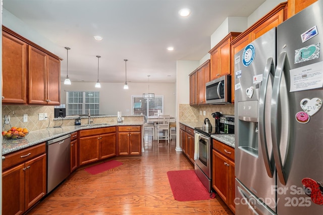 kitchen featuring decorative light fixtures, sink, light stone counters, kitchen peninsula, and stainless steel appliances