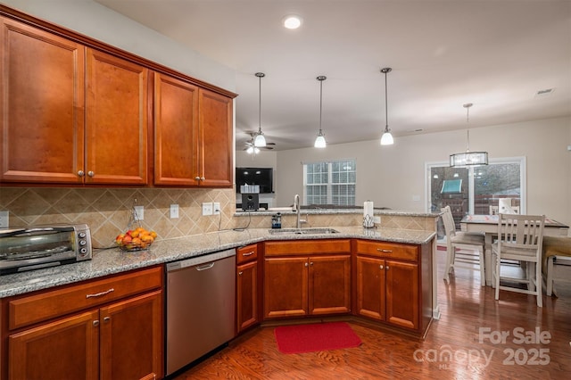 kitchen featuring decorative light fixtures, sink, stainless steel dishwasher, light stone counters, and kitchen peninsula