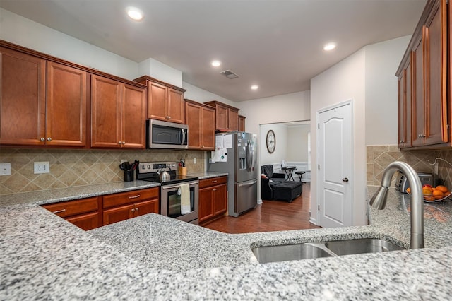 kitchen featuring sink, light stone counters, wood-type flooring, stainless steel appliances, and backsplash