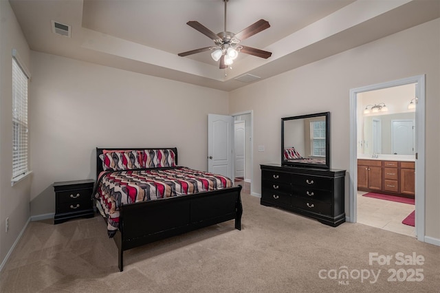 carpeted bedroom with a raised ceiling, ensuite bathroom, and ceiling fan