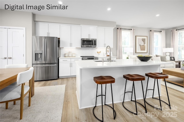 kitchen with stainless steel appliances, an island with sink, sink, and white cabinetry