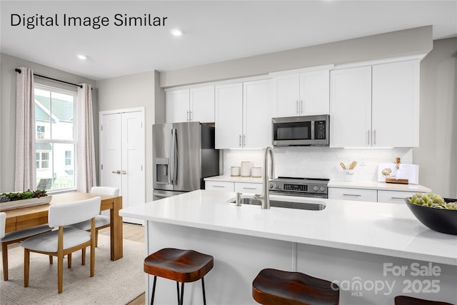 kitchen with sink, white cabinetry, backsplash, stainless steel appliances, and a kitchen bar