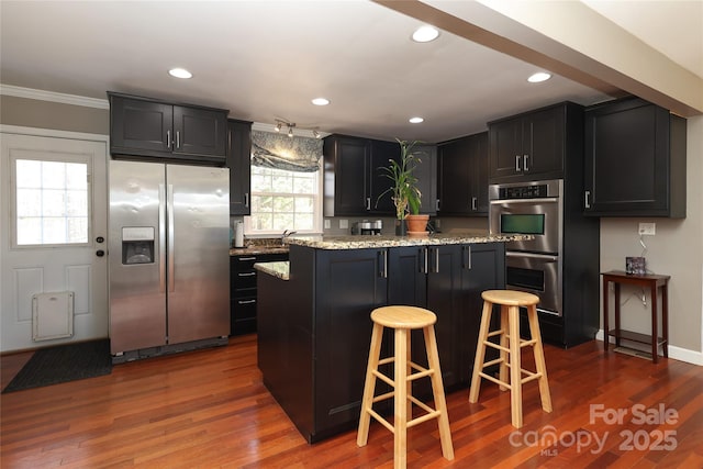 kitchen featuring a breakfast bar area, dark hardwood / wood-style flooring, a kitchen island, stainless steel appliances, and light stone countertops