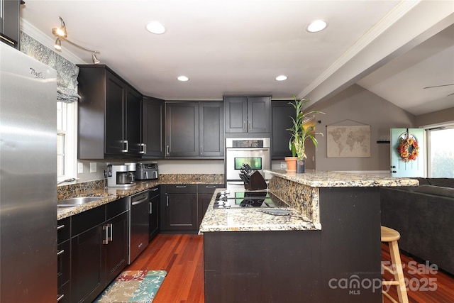 kitchen featuring dark wood-type flooring, light stone counters, appliances with stainless steel finishes, a kitchen breakfast bar, and a kitchen island