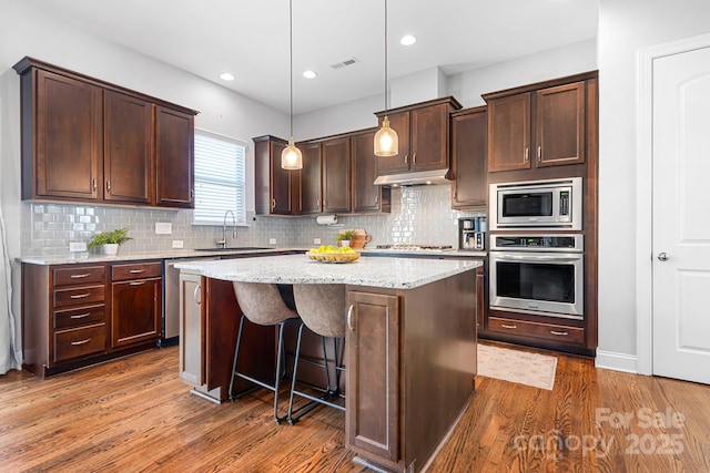 kitchen with sink, light stone counters, decorative light fixtures, a kitchen island, and stainless steel appliances