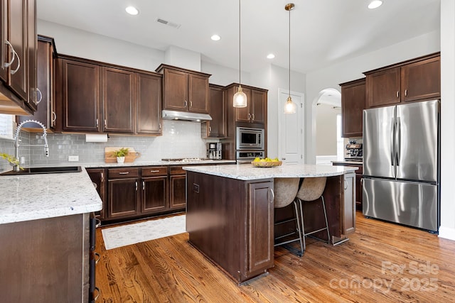 kitchen with dark wood-type flooring, sink, light stone counters, appliances with stainless steel finishes, and a kitchen island