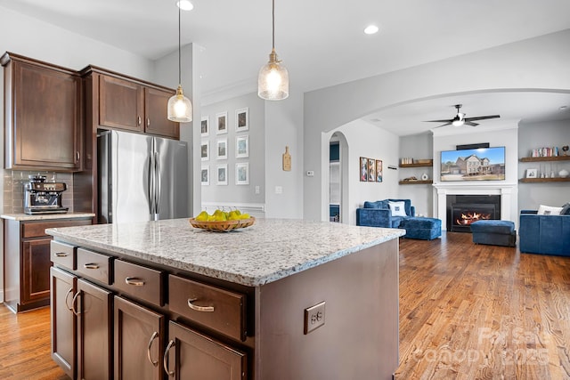 kitchen featuring decorative light fixtures, stainless steel fridge, a center island, light stone counters, and dark brown cabinets