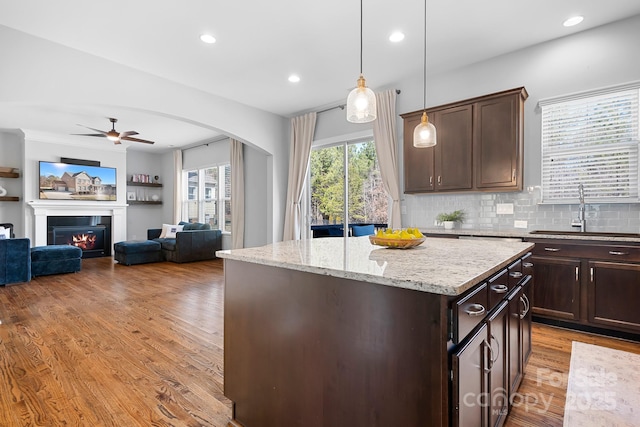 kitchen with sink, a center island, hanging light fixtures, light hardwood / wood-style flooring, and light stone countertops