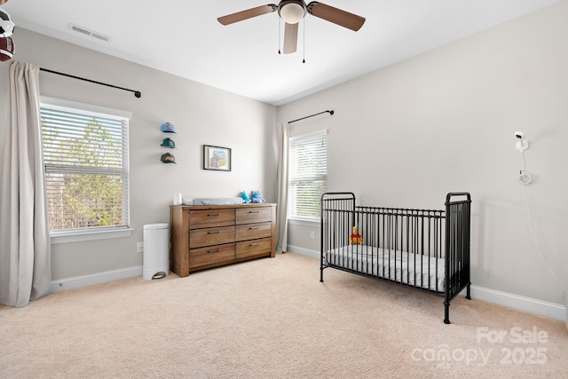 carpeted bedroom featuring a nursery area and ceiling fan