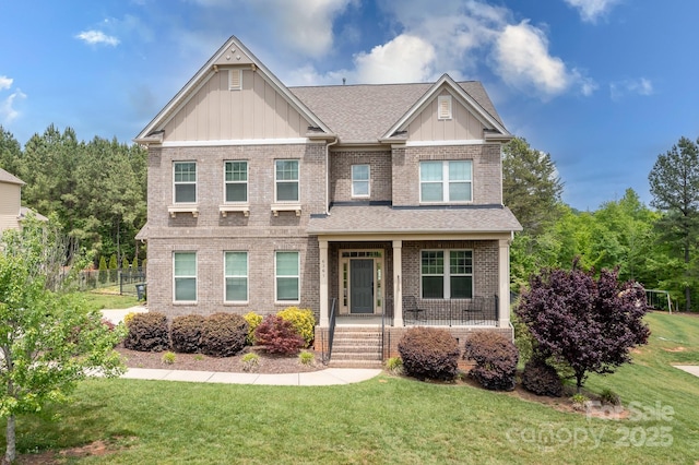 craftsman-style home with covered porch, board and batten siding, a front yard, and brick siding