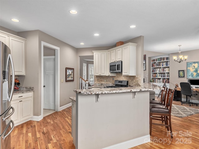 kitchen with a breakfast bar, light stone counters, white cabinetry, appliances with stainless steel finishes, and kitchen peninsula