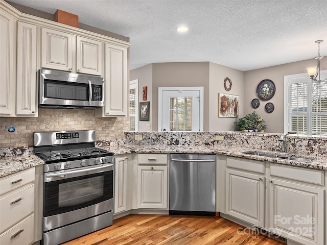 kitchen with stainless steel appliances, sink, backsplash, and light wood-type flooring