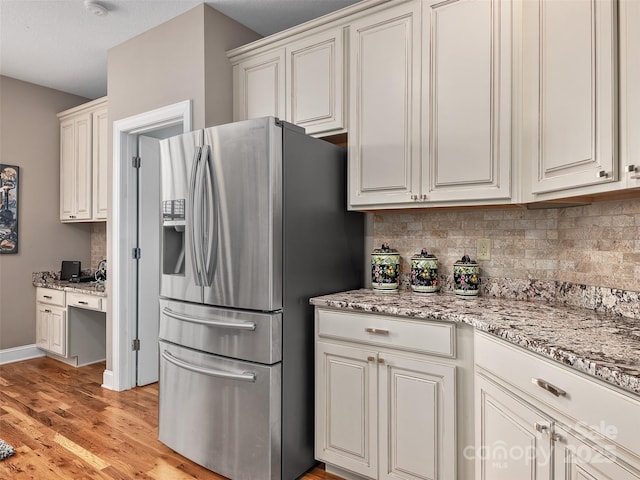 kitchen with white cabinetry, built in desk, stainless steel fridge, and decorative backsplash