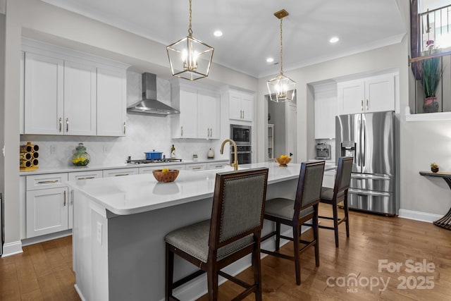 kitchen with appliances with stainless steel finishes, a kitchen island with sink, white cabinets, and wall chimney exhaust hood