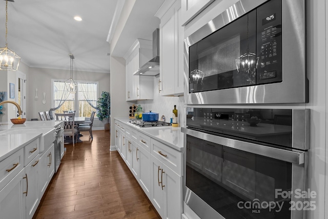 kitchen with white cabinetry, appliances with stainless steel finishes, decorative light fixtures, and wall chimney exhaust hood