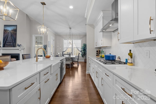 kitchen with appliances with stainless steel finishes, a chandelier, hanging light fixtures, light stone counters, and wall chimney exhaust hood