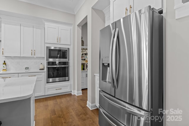 kitchen featuring dark wood-type flooring, crown molding, white cabinets, stainless steel appliances, and backsplash