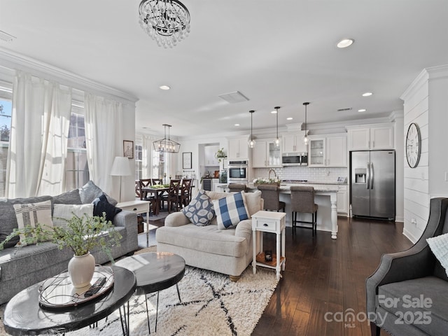 living room featuring an inviting chandelier, ornamental molding, and dark hardwood / wood-style flooring