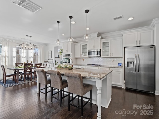 kitchen with a kitchen island with sink, hanging light fixtures, white cabinetry, and appliances with stainless steel finishes