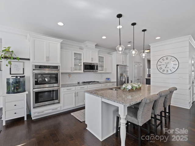 kitchen featuring light stone countertops, appliances with stainless steel finishes, a kitchen island with sink, and white cabinets